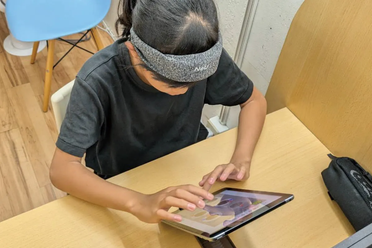 頭に脳活動センサーを装着しタブレットで学習する子ども